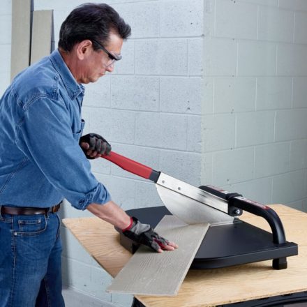 A construction worker wearing a jean jacket and pants cutting a piece of fiber cement board at an angle with Malco's FCC7 guillotine