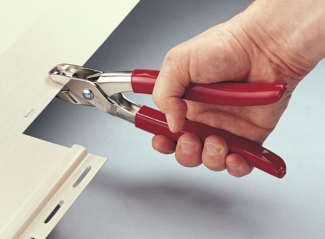 A Malco notching tool being used to create small notches on a piece of tan vinyl siding